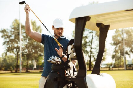 handsome-male-golfer-taking-clubs-from-bag-golf-cart